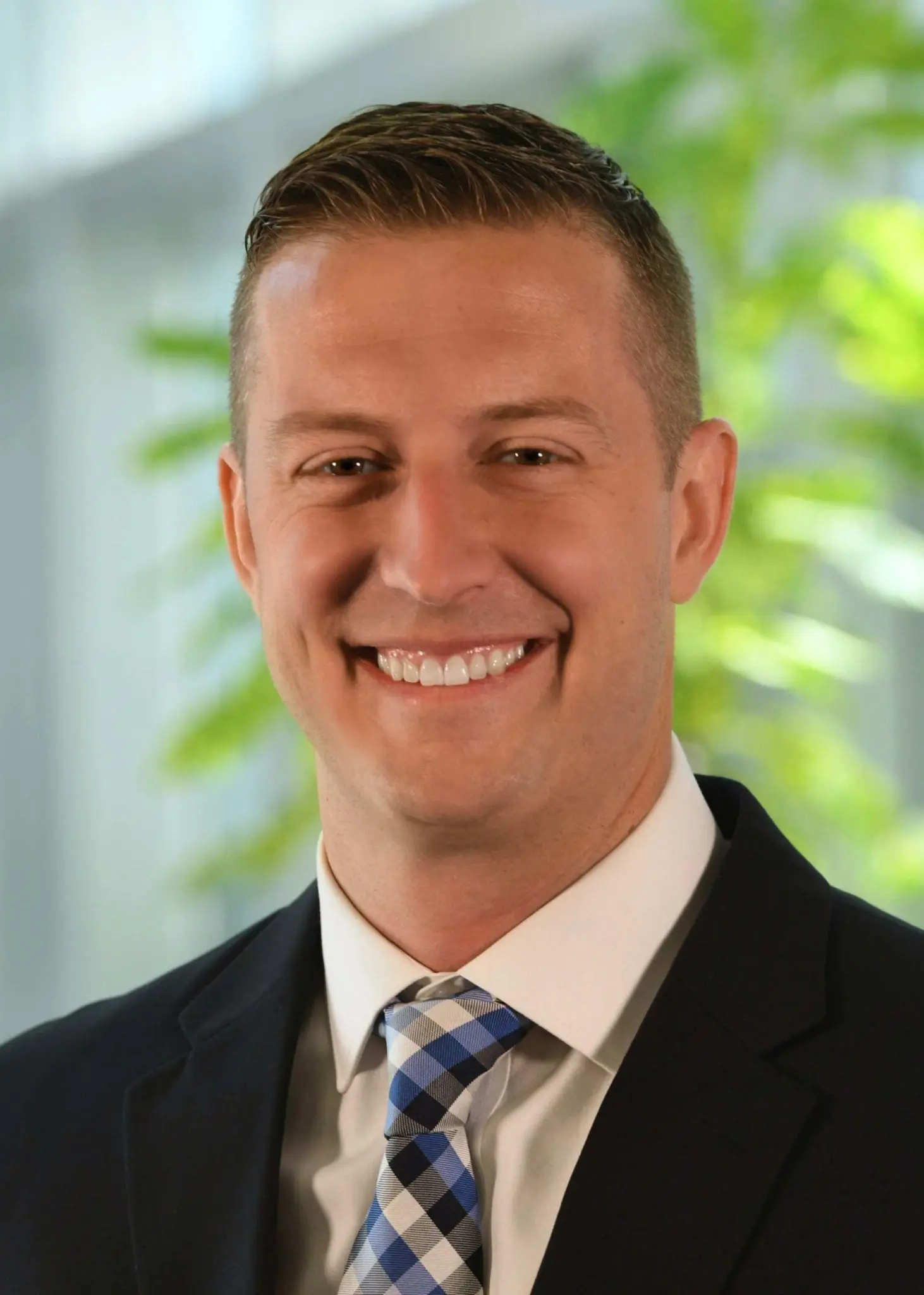 Prime's Recruiting Manager Travis Bacon, smiling while wearing a black suit with a blue & black tie.